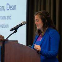 woman in blue blazer and striped dress speaks into microphone on podium with the GVSU logo